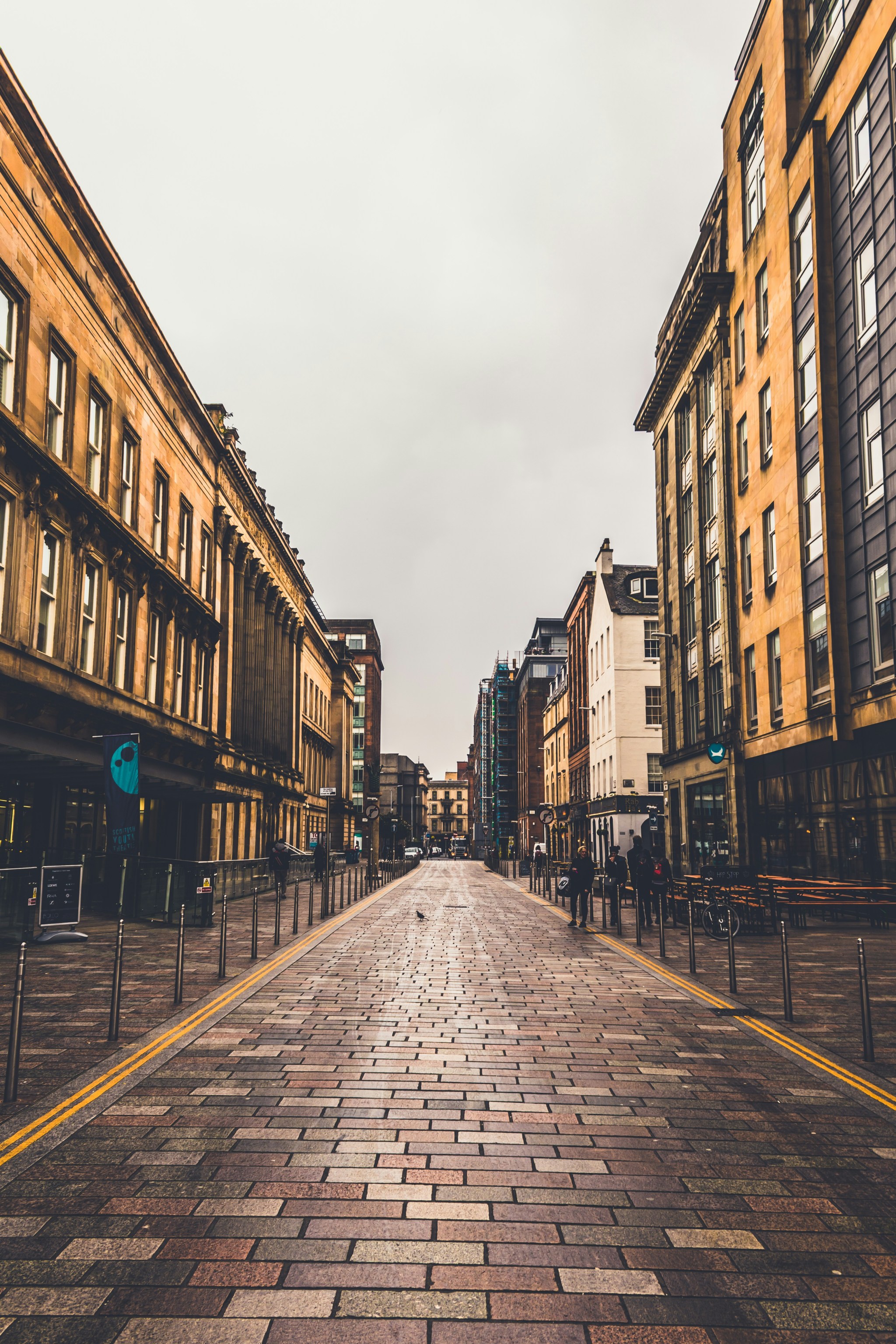 Photo of a European high street at eye level. There is a combination of old and new buildings, and some people walking around.